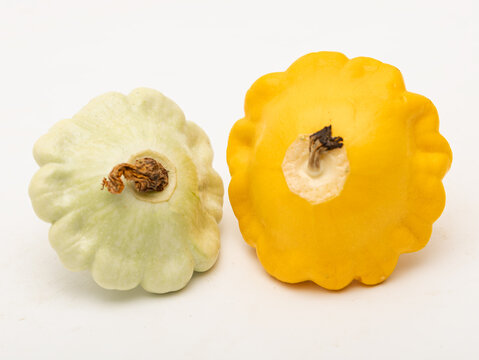 Two pattypan squash sit side by side on a white surface