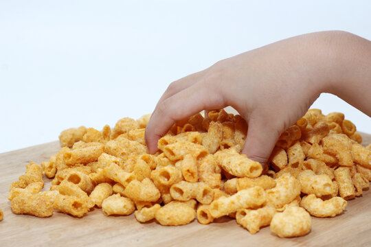 child's hand reaching down to grab a pile of crispy, seasoned fried macaroni snacks resting on a wooden board.