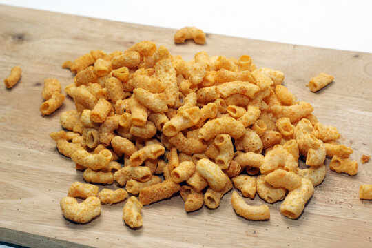 A wide shot of a mound of crunchy, seasoned macaroni snacks scattered on a flat wooden cutting board