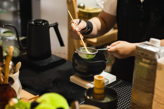 Barista sifting matcha powder using a traditional bamboo scoop.