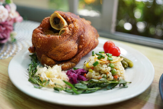 German pork knuckle with rice and garlic vegetables, served in the kitchen to restaurant customers.
