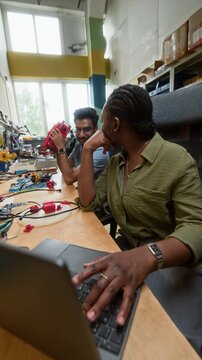 Vertical video of African American woman engineer typing on laptop and discussing robotics project with Indian colleague. Clip is ideal for tech startup recruitment and STEM education promos