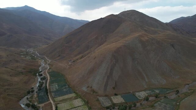 Drone view of Chalus Road terraces and fields stepping down a mountain valley beside a slim green watercourse and dry ridges. Ideal for travel, tourism, and nature stock Iran Alborz valleys.