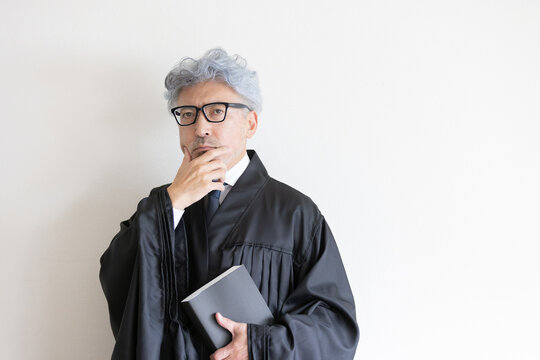 法服姿で本を持ちながら判決について考える男性裁判官
