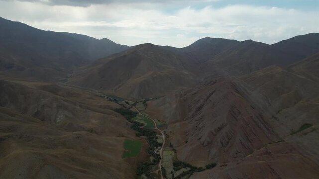 Overcast aerial of Chalus Road peaks and a vegetated valley crease between brown mountains under a layered cloudy highland sky. Ideal for travel, tourism, and nature stock Iran Alborz.