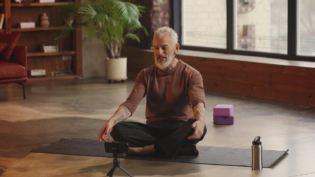 Stylish middle-aged male yoga coach records fitness video blog on phone