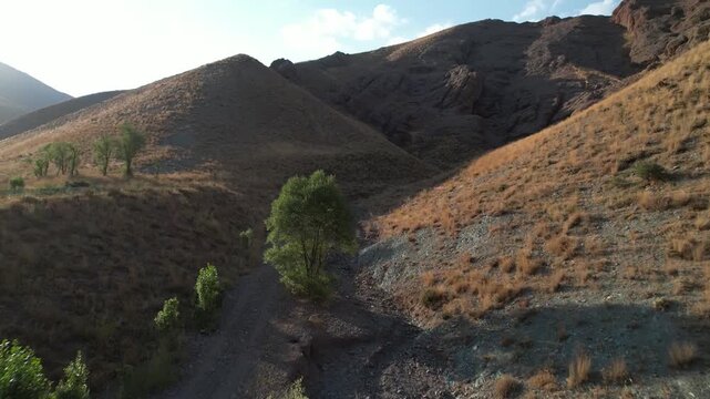 Narrow dirt track on Chalus Road climbs dry brown hills with sparse trees, a remote mountain path through arid Iranian land. Ideal for travel, tourism, and nature stock Iran Alborz valleys.