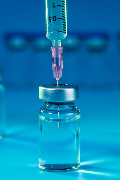 medical syringe with needle next to vaccine medicine glass vials on blue background as a conceptual backdrop for pharmaceutical research healthcare immunization biotechnology and clinical science