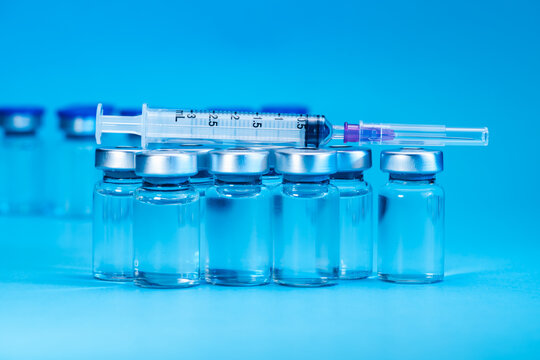 medical syringe with needle next to vaccine medicine glass vials on blue background as a conceptual backdrop for pharmaceutical research healthcare immunization biotechnology and clinical science