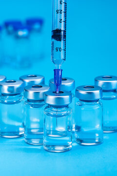 medical syringe with needle next to vaccine medicine glass vials on blue background as a conceptual backdrop for pharmaceutical research healthcare immunization biotechnology and clinical science