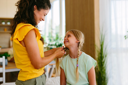 Smiling young girl looking at her mother while having her hair braided at home