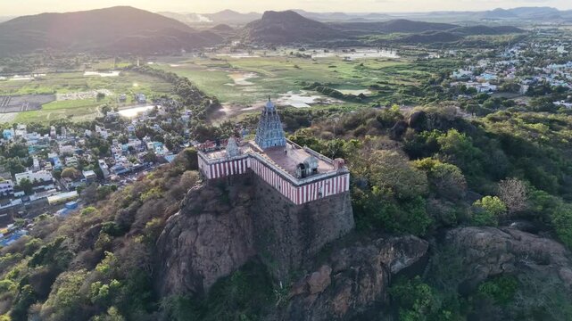 Aerial drone view of an ancient Hindu temple perched dramatically on top of a majestic mountain in India, surrounded by lush green valleys, rugged rocky peaks, with a breathtaking pan