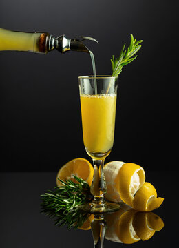 Traditional Italian liqueur Limoncello with rosemary twig on a black reflective background.