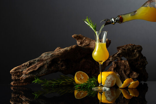 Traditional Italian liqueur Limoncello on a black reflective background.