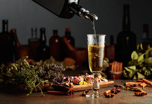 Yellow herbal liquor or mixture is poured from a vintage bottle into a glass.