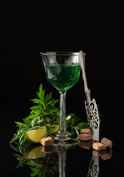 Glass of absinthe with ingredients on a black background.