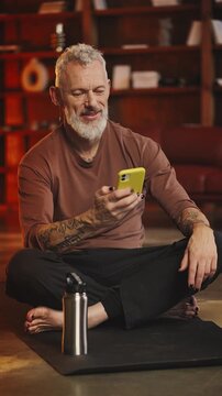 Happy toned man in his 50s checks fitness app on phone after home workout