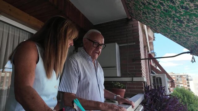 Caregiver assisting elderly man with paperwork on balcony