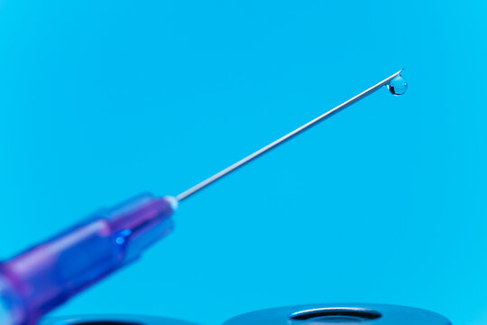 medical syringe with needle next to vaccine medicine glass vials on blue background as a conceptual backdrop for pharmaceutical research healthcare immunization biotechnology and clinical science