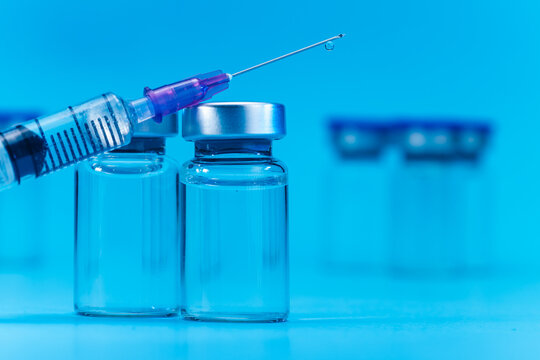 medical syringe with needle next to vaccine medicine glass vials on blue background as a conceptual backdrop for pharmaceutical research healthcare immunization biotechnology and clinical science
