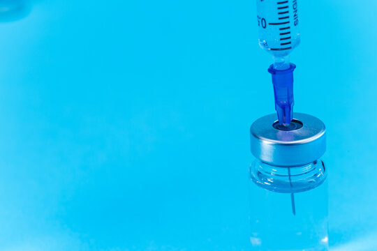 medical syringe with needle next to vaccine medicine glass vials on blue background as a conceptual backdrop for pharmaceutical research healthcare immunization biotechnology and clinical science