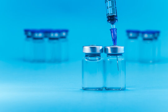 medical syringe with needle next to vaccine medicine glass vials on blue background as a conceptual backdrop for pharmaceutical research healthcare immunization biotechnology and clinical science