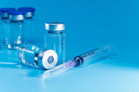 medical syringe with needle next to vaccine medicine glass vials on blue background as a conceptual backdrop for pharmaceutical research healthcare immunization biotechnology and clinical science