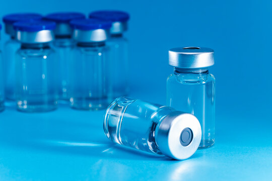 medical syringe with needle next to vaccine medicine glass vials on blue background as a conceptual backdrop for pharmaceutical research healthcare immunization biotechnology and clinical science