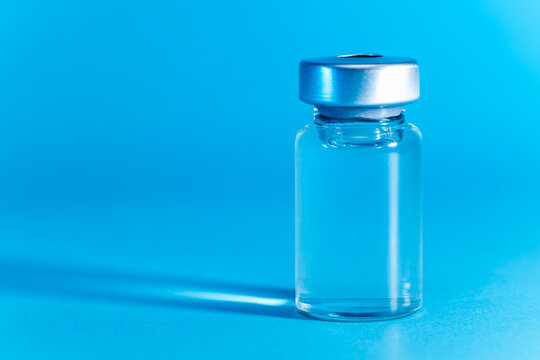 medical syringe with needle next to vaccine medicine glass vials on blue background as a conceptual backdrop for pharmaceutical research healthcare immunization biotechnology and clinical science