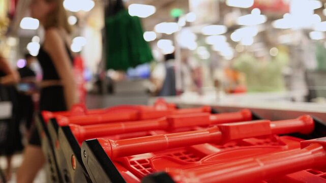 Close-up of nested red shopping carts or baskets lined up in a row against the blurred background of checkout counters in a grocery store or supermarket. Retail shopping, commerce concept.