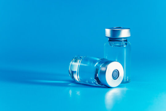 medical syringe with needle next to vaccine medicine glass vials on blue background as a conceptual backdrop for pharmaceutical research healthcare immunization biotechnology and clinical science
