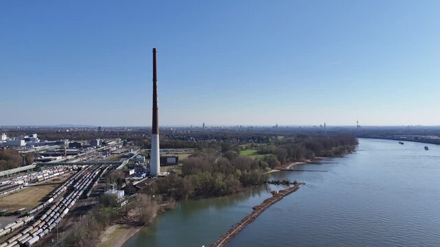 Drone flies forward toward the Bayer tower with the Rhine and industrial rail lines visible from an elevated angle.