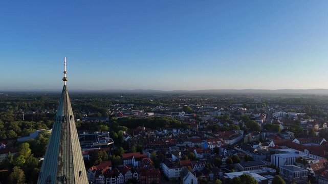 Close aerial orbit circles the cathedral spire and distinctive double cross while the Paderborn cityscape shifts across the background.