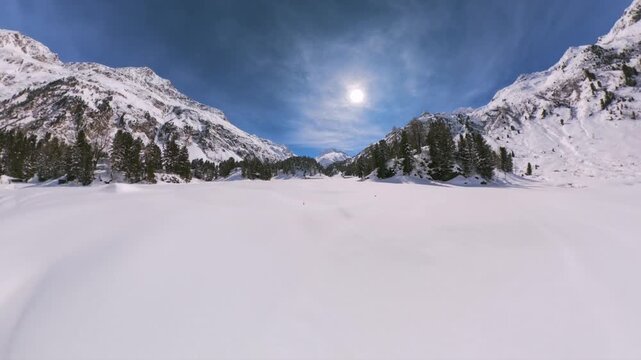 Snow-covered frozen Lake Cavloc surrounded by alpine mountains in Maloja, Switzerland. Aerial forward low flight