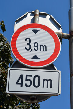 A round height limit road sign with a red border indicating three point nine meters clearance located four hundred and fifty meters ahead against a bright blue sky.