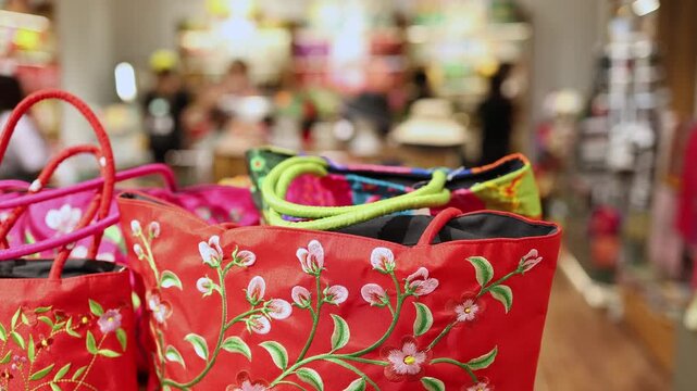 Close-up of bright red fabric bags or totes with delicate embroidered floral vine patterns on display in a souvenir shop, gift store or boutique. Retail shopping and traditional accessories.