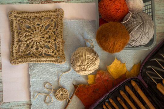 Cozy autumn craft flat lay with a beige crocheted granny square, yarn ball, wooden crochet hooks set, and unfinished motif on rustic wood background. Perfect for DIY handcraft blogs.