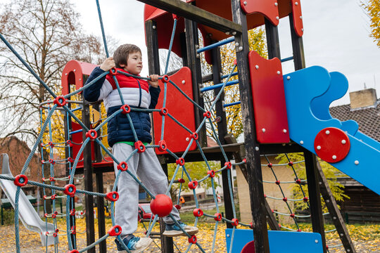 Child boy climbing rope net at playground in autumn