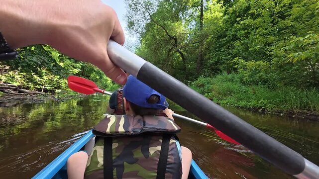 People paddling in a kayak on a narrow river through a lush green forest. Summer adventure family Kayak trip. Active lifestyle, weekend pastime. Outdoor recreation. High quality 4k footage.