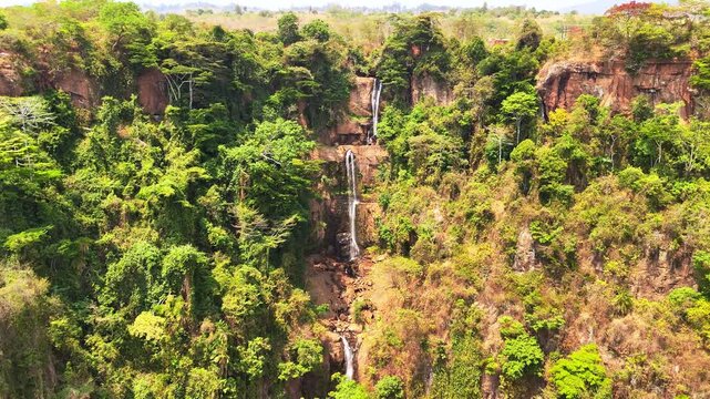 Wide drone view tilts upward across three levels of Manchewe Falls, revealing the scale of the U-shaped forested escarpment in Malawi.