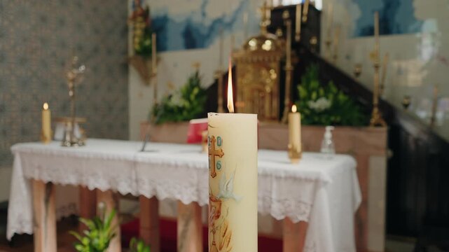 Decorated easter candle burning in front of an altar with gold tabernacle and flowers