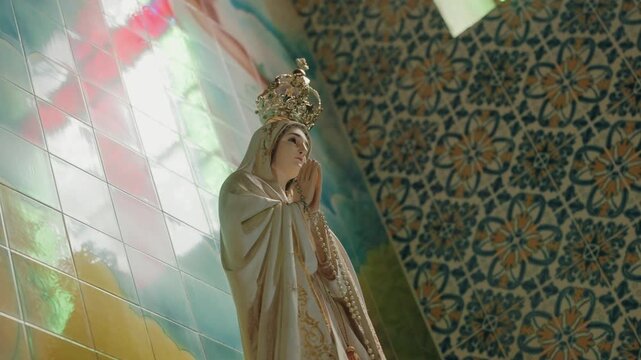 Praying Madonna figure with golden crown and rosary against painted and patterned tiles