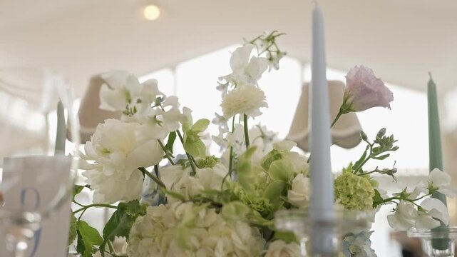 Hydrangeas roses and lisianthus arranged between pale candles in a light filled marquee