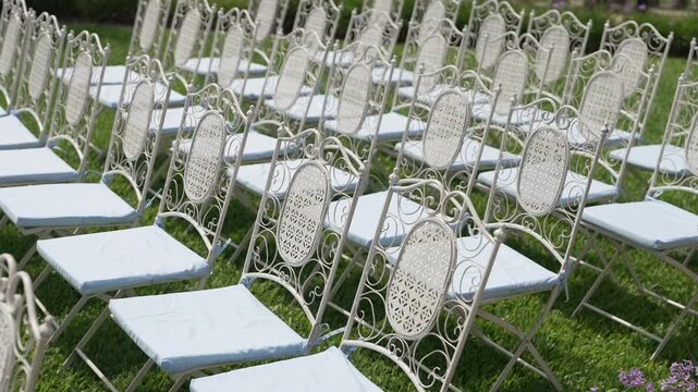 Empty ornate metal chairs with white cushions lined up on a sunny garden lawn