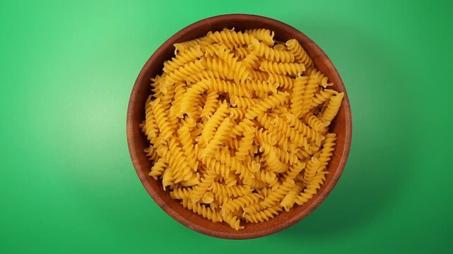 Rotation of fusilli pasta in a wooden bowl close-up on a greem background. Top view