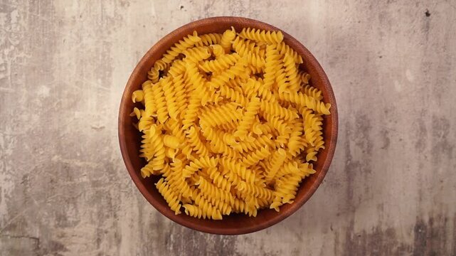 Rotation of fusilli pasta in a wooden bowl close-up on a concrete background. Top view
