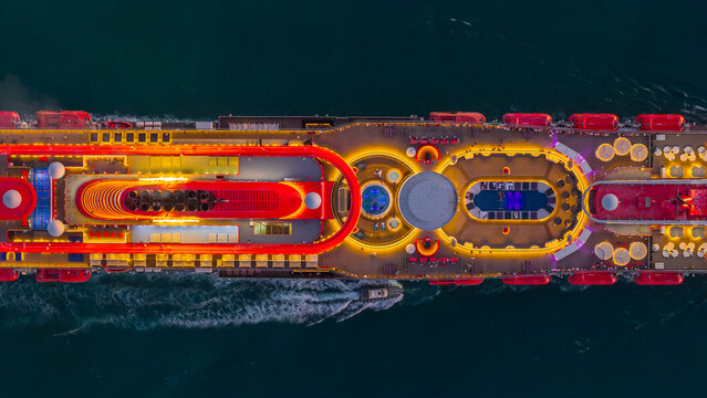 Aerial view of the illuminated decks and swimming pools of a large cruise ship navigating near Porto Civitavecchia, Civitavecchia, Lazio, Italy.