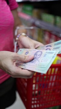 Close up view of woman hands counting cash money Vietnamese dong (VND) banknotes for shopping in supermarket. Calculating budget to spend in grocery store. Financial planning in Vietnam concept.