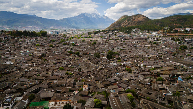 Aerial view of Lijiang Old Town featuring a dense expanse of traditional dark-tiled rooftops and narrow streets set against a backdrop of mountains in Lijiang, Yunnan, China.