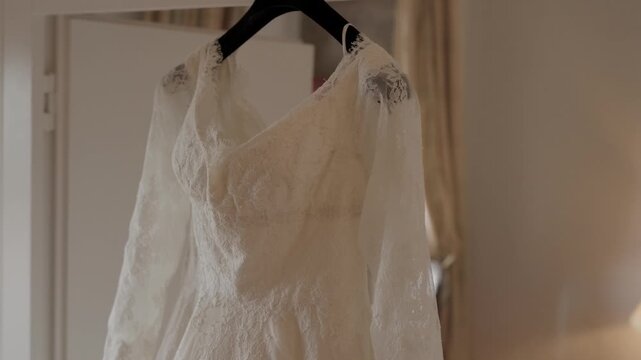 Bridal Gown With Lace Sleeves And Beaded Shoulders Hanging On A Hanger In A Bright Bedroom
